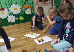 Dzieci siedzą w kole. Odzwierciedlają klockami Lego wzór podany na kartce . Zabawa w kodowanie