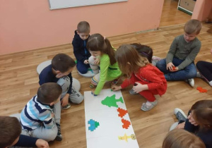 Dzieci siedzą w kole i wykonują zadanie z kodowania.