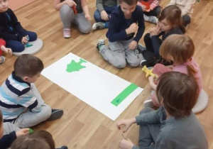 Dzieci siedzą w kole i wykonują zadanie z kodowania