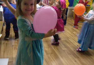 Dzieci tańczą z kolorowymi balonami. Na pierwszym planie Helenka pozuje trzymając w ręku różowy balon.
