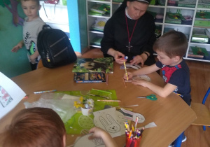 Dzieci na lekcji religii. Wycinają zajączka wielkanocnego, a następnie malują i łączą elementy za pomocą kleju. Z dziećmi przy stoliku siedzi siostra zakonna.