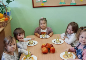 Dzieci siedzą przy stoliku, jedzą przygotowane przez siebie owocowe smakołyki.