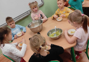 Przedszkolaki z grupy 3 siedzą przy stolikach. Dzieci jedzą wykonana przez siebie sałatkę owocową.