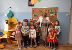 Zdjęcie grupowe przedszkolaków z grupy 2 z wychowawczynią. Dzieci mają na sobie stroje nawiązujące do jesieni : naszyjniki z kasztanów, liście naszyte na ubraniach, strój wiewiórki.