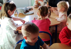 Dzieci siedzą przy stolikach, wykonując kota z rolki po papierze toaletowym. Obklejają rolkę papierem w wybranym przez siebie kolorze - białym, czarnym lub brązowym. Następnie doklejają oczy, wąsy , nos i ogon. Dzieciom w pracy pomaga pani psycholog.