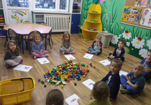 Dzieci siedzą w kole. Odzwierciedlają klockami Lego wzór podany na kartce . Zabawa w kodowanie.