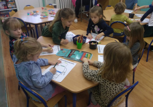 Dzieci siedzą przy stoliku. Kolorują Ludzika Lego.