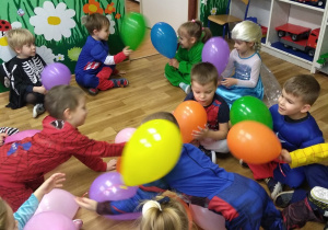 Dzieci siedzą trzymając kolorowe balony.
