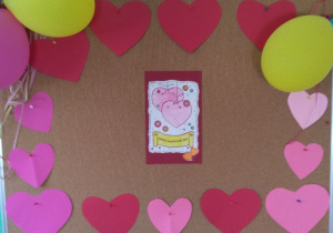 Walentynkowa dekoracja tablicy w grupie 2. Pośrodku kartka z 2 nakładającymi się sercami. Kartka otoczona sercami w kolorze czerwonym i różowym.