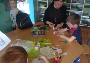 Dzieci na lekcji religii. Wycinają zajączka wielkanocnego, a następnie malują i łączą elementy za pomocą kleju. Z dziećmi przy stoliku siedzi siostra zakonna.