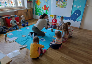 Dzieci siedzą w kole i malują farbami rysunki pisanek.