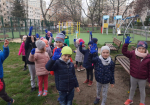 Dzieci na zewnątrz przedszkola, mają założone rękawiczki. Uczestniczą w akcji "Sprzątanie Świata".