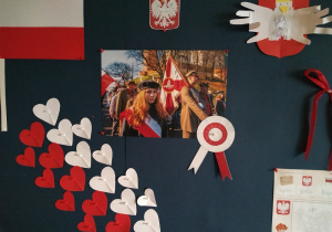 Dekoracja w grupie drugiej. Na dużej tablicy korkowej wywieszone : flaga Polski, serduszka w barwach białych i czerwonych, godło Polski, wzór godła Polski, które dzieci wykonywały podczas zajęć.