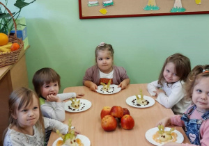 Dzieci siedzą przy stoliku, jedzą przygotowane przez siebie owocowe smakołyki.