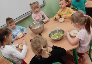 Przedszkolaki z grupy 3 siedzą przy stolikach. Dzieci jedzą wykonana przez siebie sałatkę owocową.