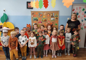 Zdjęcie grupowe przedszkolaków z grupy 2 z wychowawczynią. Dzieci mają na sobie stroje nawiązujące do jesieni : naszyjniki z kasztanów, liście naszyte na ubraniach, strój wiewiórki.