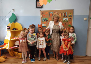 Zdjęcie grupowe przedszkolaków z grupy 2 z wychowawczynią. Dzieci mają na sobie stroje nawiązujące do jesieni : naszyjniki z kasztanów, liście naszyte na ubraniach, strój wiewiórki.