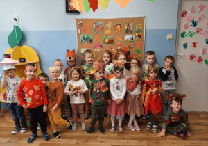 Zdjęcie grupowe przedszkolaków z grupy 2. Dzieci mają na sobie stroje nawiązujące do jesieni : naszyjniki z kasztanów, liście naszyte na ubraniach, strój wiewiórki.